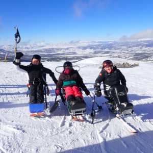 three sit skiers wave from the top of the ski slope